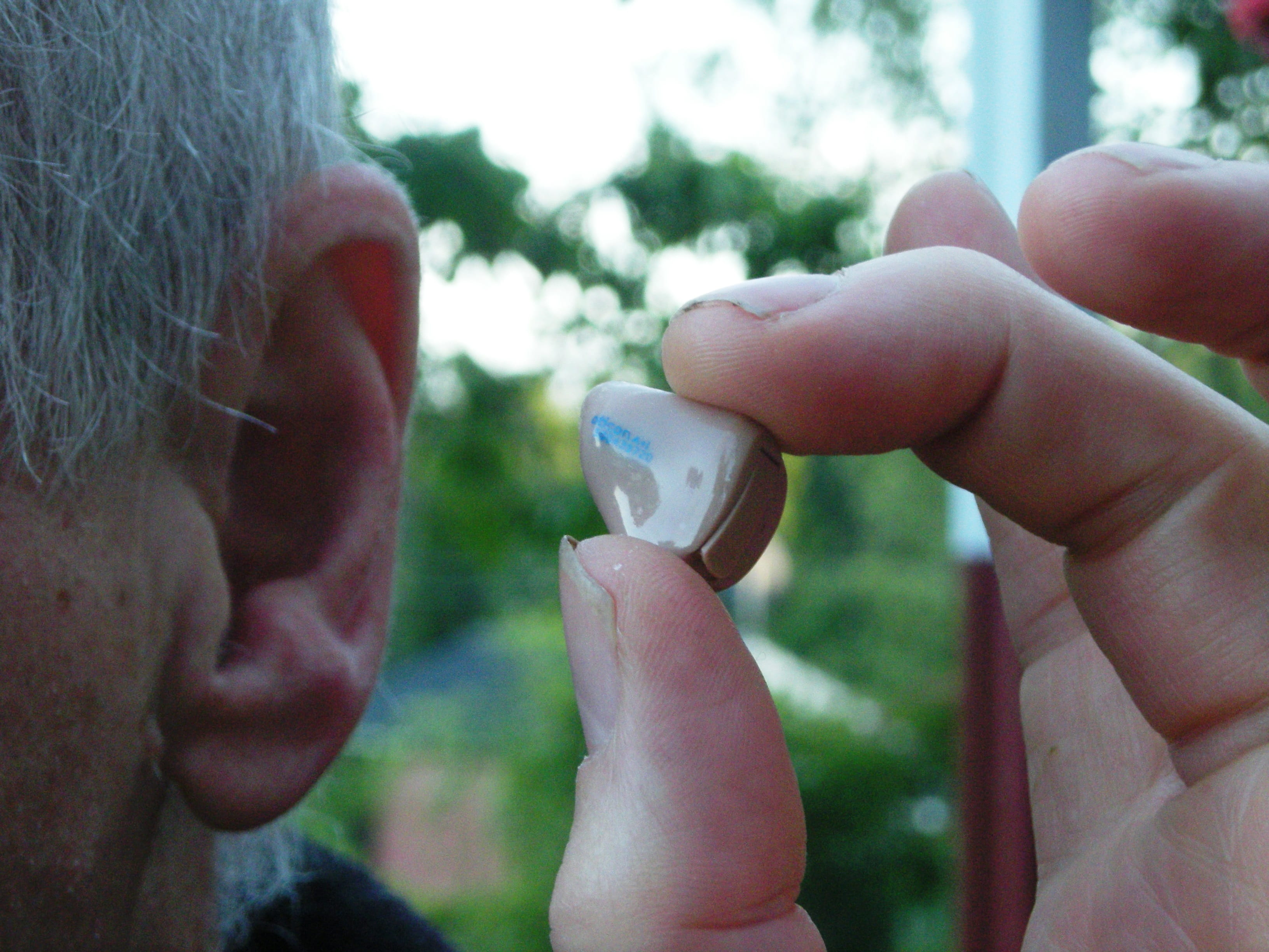 Elderly man holding hearing aid next to ear.