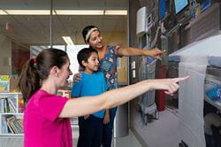 Child Life specialist stands in front of a picture talking to a mother and son about his upcoming surgery