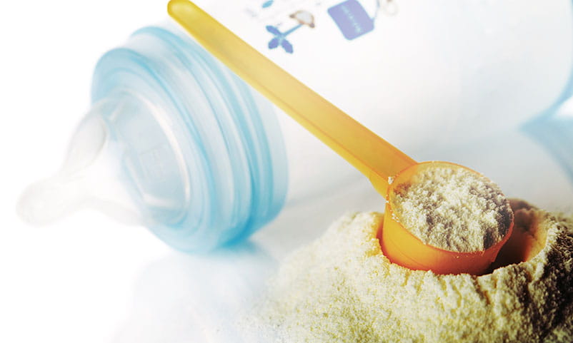 Closeup of a baby bottle and a scoop of formula.