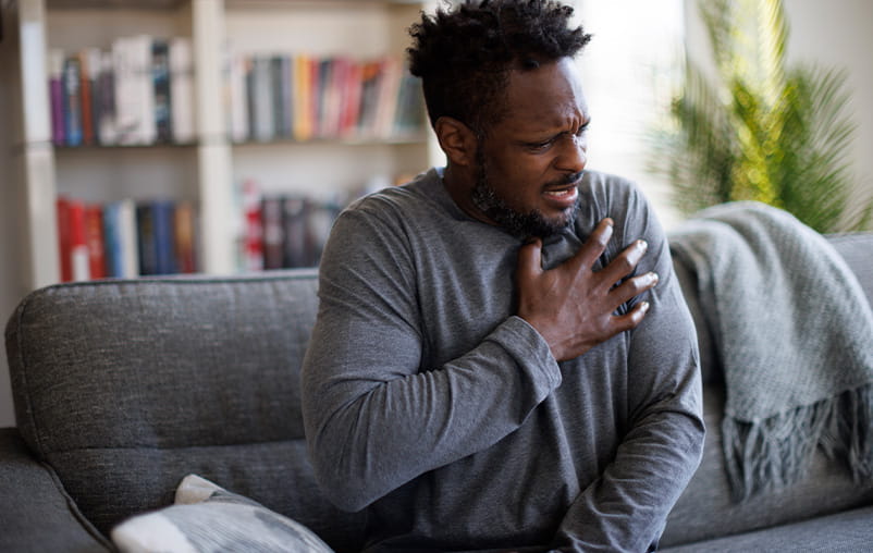 A man sits on a couch and clutches his chest in pain.