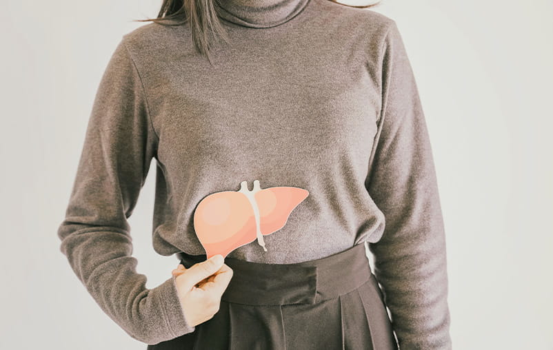 A woman holds an illustrated liver in front of her abdomen.
