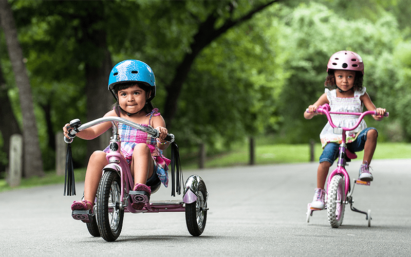 Two Hispanic toddler girls riding their bikes on the street.