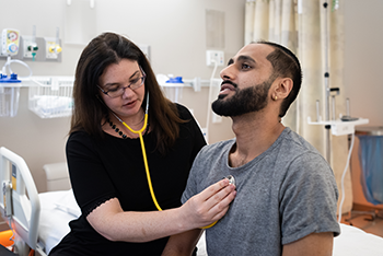 A nurse is listening to the heartbeat of a young man in the Adolescent and Young Adult program.