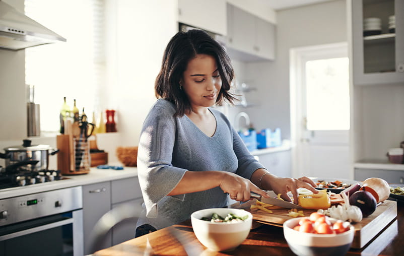 A woman chops vegetables in the kitchen.