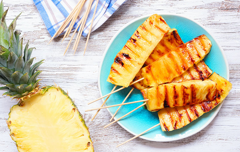 Brazilian grilled pineapple on spears on a blue plate.