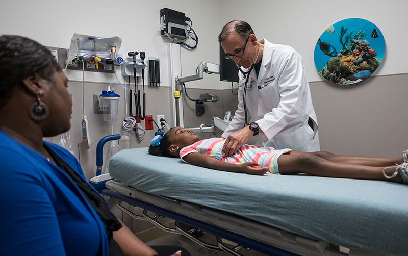 University Health emergency department provider examines a young girl’s abdomen while her mother looks on.