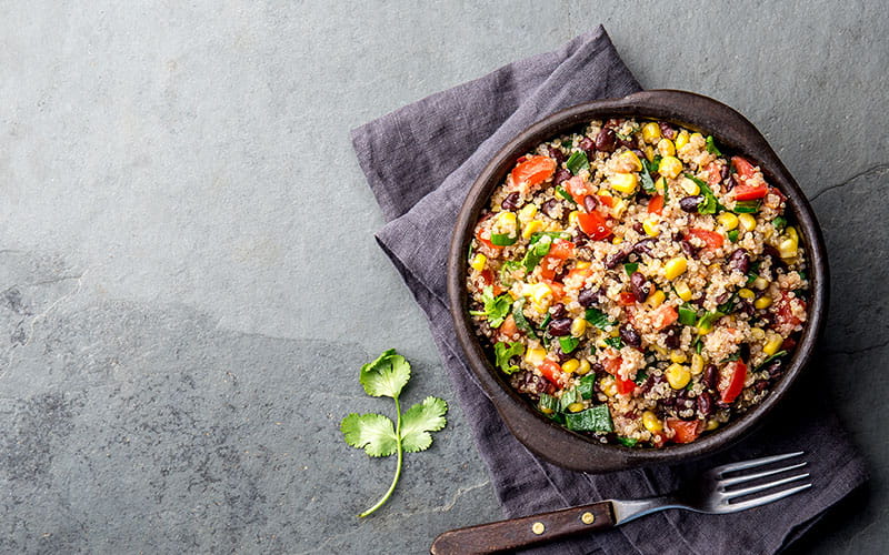 Mexican black bean corn quinoa salad in clay bowl top view, copy space.