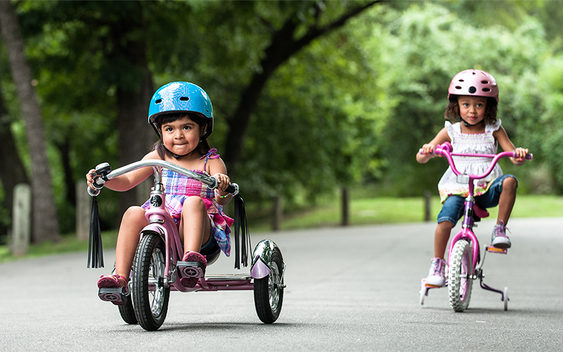 Two Hispanic toddler girls riding their bikes on the street.
